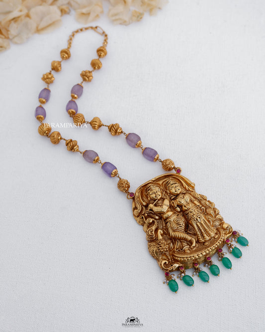 This handcrafted temple necklace showcases a depiction of Lord Krishna and Radhe, crafted with pure silver and enhanced with micron gold plating and semi-precious beads.
